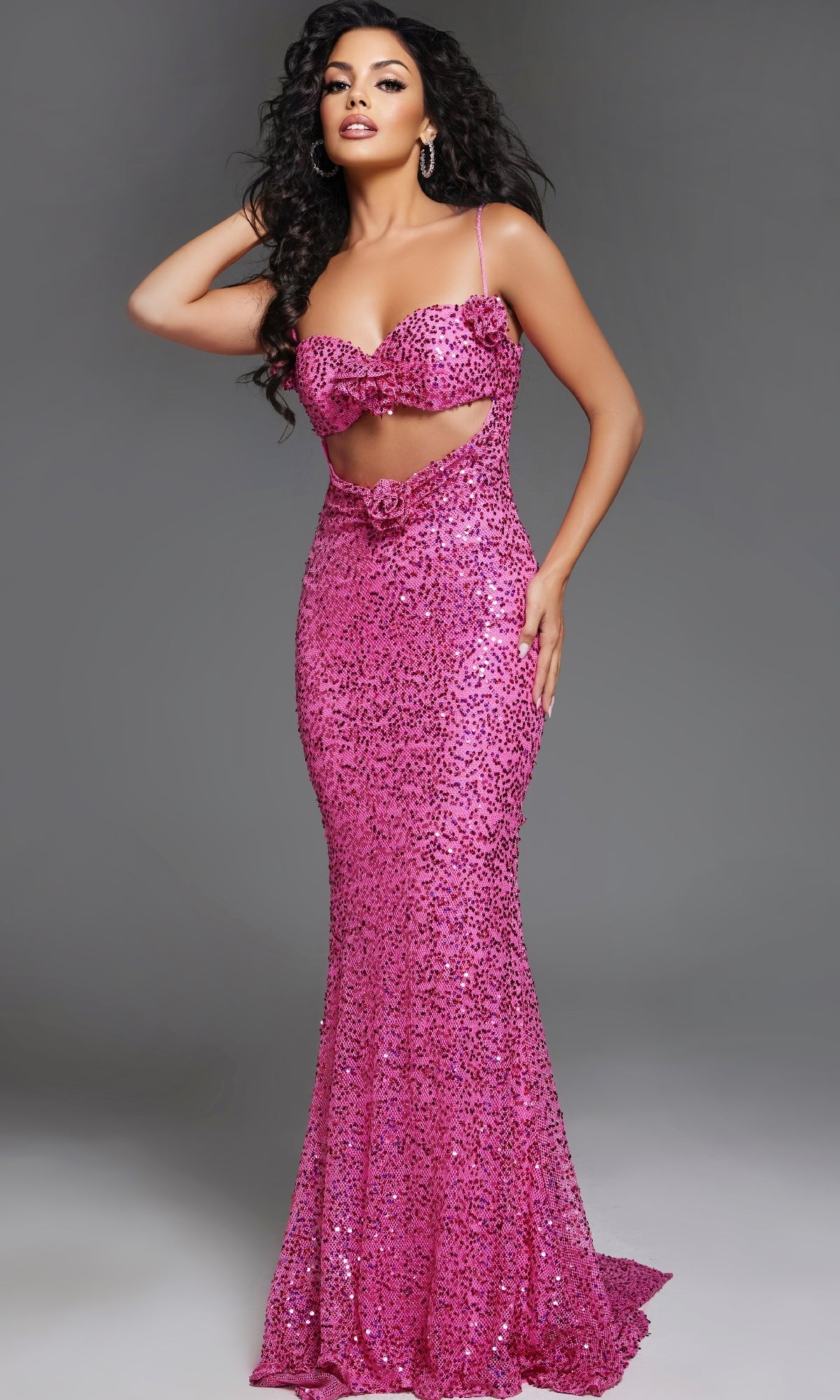 A woman poses in the Hot Pink Strapless Sequin Prom Gown: Jovani D5403, a fitted, floor-length dress featuring a front cutout and bow details, set against a plain gray background.